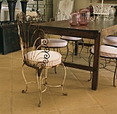 Simple, antique wooden table and elaborate, vintage metal chairs on tiled floor