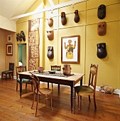 Esszimmertisch vor gelbe Wand mit afrikanischen Skulpturen und Masken