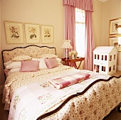Doppelbett mit geblümtem Bettbezug vor altes Puppenhaus
