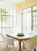 Holztisch und weiße Schalenstühle vor große Sprossenfenster