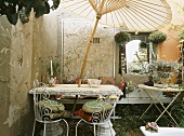 Gartenmöbel und asiatischer Sonnenschirm im Tisch vor bemalte Betonwand im Innenhof eines Hauses
