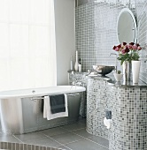 Modernes Designerbad mit wellenförmigem Waschtisch aus grauen Mosaikfliesen und freistehende Badewanne in Metall-Optik