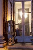 Mädchen steht an der Fenstertür eines weihnachtlich geschmückten Hauses