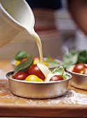 Pouring egg and milk mixture into individual tomato quiche