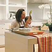 Mutter und Tochter in der Küche, Kind hält Deckel eines Kochtopfs