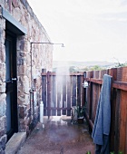 Einfache Dusche im Aussenbereich eines rustikalen Steinhauses mit Sichtschutz aus Holz