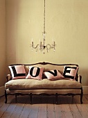 Rosa Kissen mit eindeutiger Botschaft auf einem barocken Sofa, darüber ein klassischer Lüster