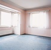 Leerstehender, stuckierter Raum mit blauem Teppichboden und rosa Wänden