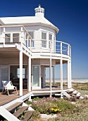 Ein strahlend weisses Haus am Meer, mitten in einer Blumenwiese