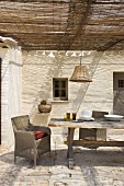 Rustikale, überdachte Terrasse mit altem Bauerntisch und Rattansessel