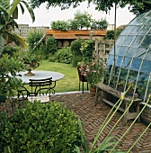 Schöne Steinterrasse und Glasanbau mit Blick auf ein kleines Nebengebäude im Garten