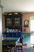 Antikes, blaues Küchenbuffet und bunt bemalter Bauerntisch im Esszimmer mit Steinboden und Wandvertäfelung