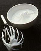 Beaten egg white in a bowl and on a whisk
