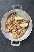 Two fried peppered plaice with lemon wedges