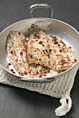 Two fried peppered plaice in an aluminium frying pan