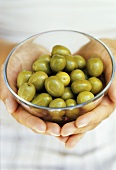 Hands holding a bowl of green olives