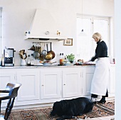 Traditionelle Küche im Landhausstil mit kochender Frau und großem, schwarzen Hund auf dem Teppich