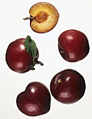 Four whole plums and half a plum against white background