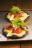 Mini pizzas topped with mushrooms, tomatoes and cured ham