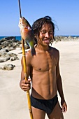 Junger Mann mit aufgespiesstem Papageienfisch am Strand