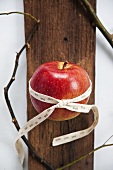 An apple tied with a days-of-the-week ribbon on a wooden surface
