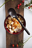 A bowl of muesli with apples and rosehip jam on a wooden surface