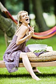 Blonde Frau bespritzt sich mit Wasser im Garten