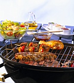 Grilled meat on the barbeque with marinade, salad and sauces in the background