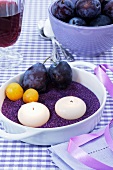 Candles, damsons and greengages on purple sand