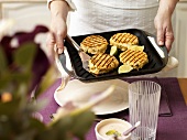 Female chef holding grill pan containing fish cakes