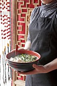 Woman holding bowl of Asian soup with jiaozi and vegetables