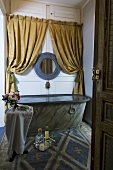 Blick durch geöffnete Tür in Badezimmer mit antiker Badewanne & schweren Stoffvorhängen