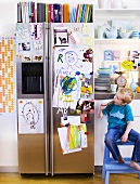 Kleiner Junge in Küche neben Kühlschrank mit Kinderbildern