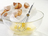 Eggs broken into glass bowl with whisk