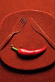 Plate covered in chilli powder with knife, fork & chilli (a face)