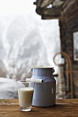 Milk can and glass of milk on table outside Alpine chalet