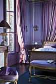 Schlafzimmer in Lilatönen mit Bett, Bettbank & bodenlangen Vorhängen im Schloss La Verrerie (Frankreich)