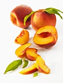 A partly-sliced peach, two whole peaches in background