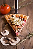 Slice of pizza with mushrooms, salami & artichokes on server
