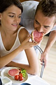 Young woman letting her boyfriend take a bite of salami sandwich
