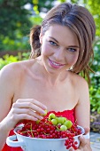 Young woman holding colander full of redcurrants & gooseberries