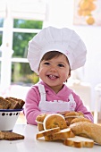 Little girl in chef's hat sitting at table with muffins