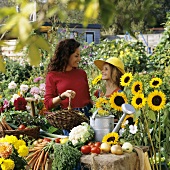 Mother and daughter among summer flowers and vegetables