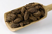 Brown cardamom pods in a wooden scoop