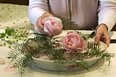 Arranging roses and coral fern in a deep plate