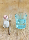 Salt shaker, fork and glass of water on wooden background