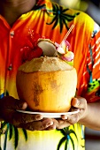 Man in colourful shirt holding a coconut drink (Seychelles)