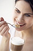 Young woman eating milk froth from latte macchiato with spoon