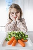 Girl sitting sadly in front of a plate of vegetables