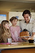 Father showing daughters how to turn a cake out of the tin